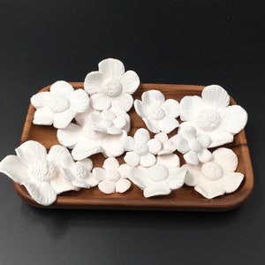 May include: A wooden tray with white ceramic flower-shaped air fresheners. The flowers are arranged in a cluster and are all different sizes.