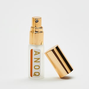 May include: A gold and clear glass bottle with a gold cap and a label that says "ANOQ". The bottle is sitting on a white surface.