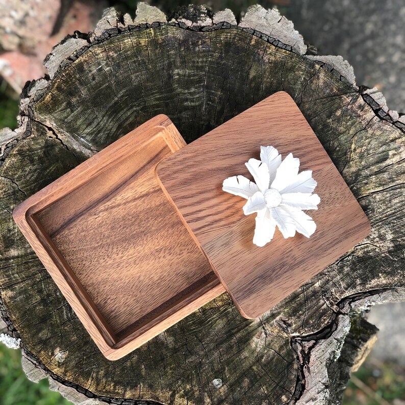 May include: A wooden box with a lid, the lid is open and a white flower is inside the box. The box is sitting on a tree stump.