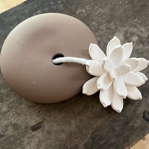 May include: A brown ceramic diffuser with a white string and a white ceramic flower on top.
