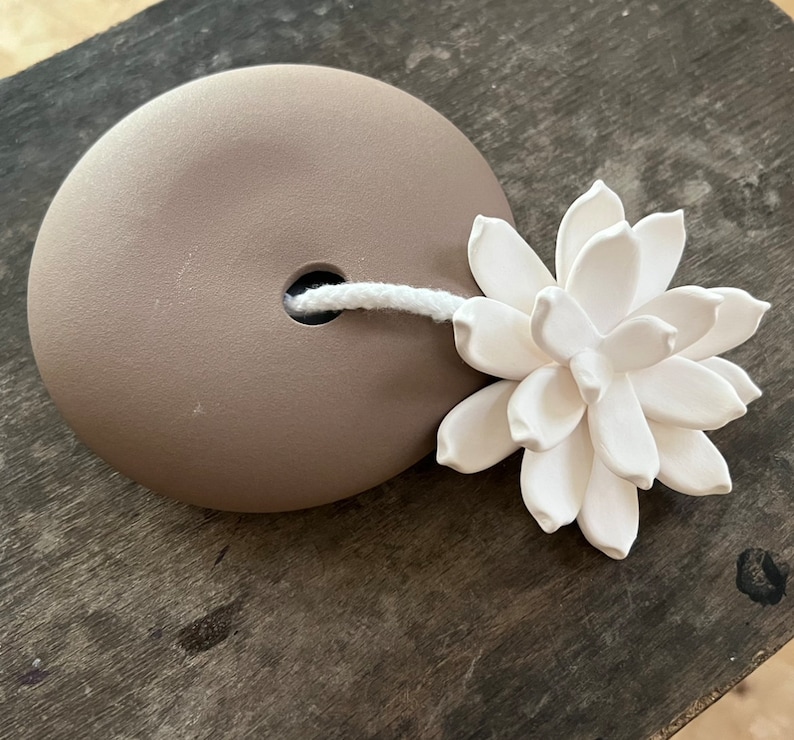 May include: A brown ceramic diffuser with a white string and a white ceramic flower on top.