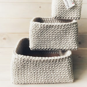 May include: Three beige crocheted storage baskets stacked on top of each other. The top basket has a white tag with the text "Handmade with love by: Nataliya".