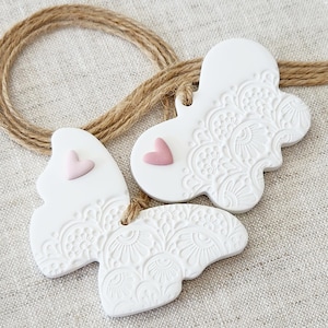May include: Two white ceramic butterfly ornaments with pink hearts. The butterflies have a delicate, embossed floral design.