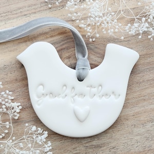 May include: White ceramic dove ornament with a gray velvet ribbon and the text "Godfather" and a small heart.
