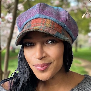 May include: A multi-colored newsboy cap with a plaid brim and a purple and blue top. The cap is made of a textured fabric and has a classic, stylish design. The cap is a fashionable accessory.