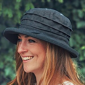Puede incluir: Una mujer con un sombrero negro de ala ancha con una corona plisada. Est&aacute; sonriendo y tiene el pelo largo y casta&ntilde;o.
