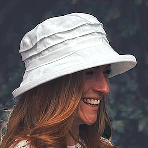 May include: A white sun hat with a wide brim and a pleated crown. The hat is made of a lightweight fabric and has a casual, relaxed style.