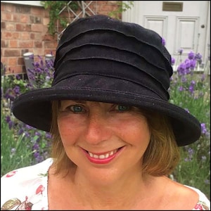 Puede incluir: Una mujer con un sombrero negro de ala ancha con una corona plisada. Est&aacute; sonriendo y tiene ojos azules.