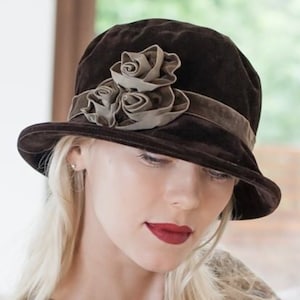 May include: A brown velvet cloche hat with a brown velvet band and a large brown and beige flower accent.