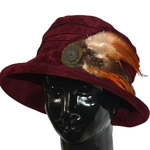 May include: A burgundy velvet cloche hat with a wide brim and a decorative button and feather embellishment.