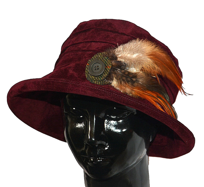 May include: A burgundy velvet cloche hat with a wide brim and a decorative button and feather embellishment.
