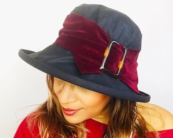 Elegante sombrero de lluvia encerado negro con elegante banda y hebilla burdeos. Se ajusta a todo tipo de cabezas. Totalmente impermeable, con ala ancha y plegable.
