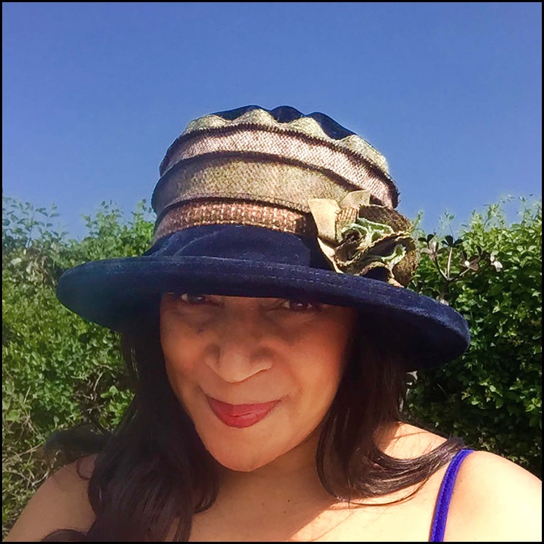 May include: A woman wearing a blue velvet hat with a multi-colored patterned brim and a green flower accent.
