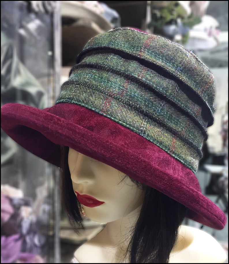 Puede incluir: Un sombrero de fieltro burdeos con una banda de cuadros verdes y negros. El sombrero tiene un ala ancha y una corona suave y flexible.