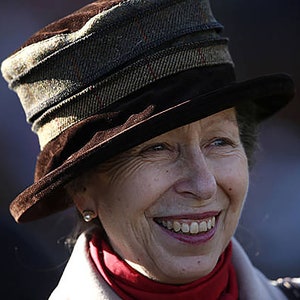Puede incluir: Una mujer con un sombrero marr&oacute;n con una banda estampada y una bufanda roja. Est&aacute; sonriendo y mirando hacia un lado.