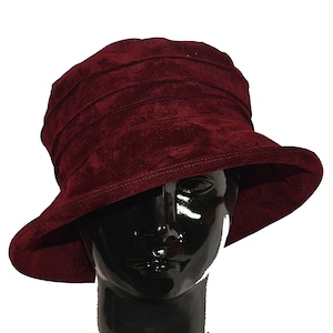 May include: A burgundy velvet cloche hat with a wide brim. The hat is folded in a series of pleats and has a simple, elegant design.