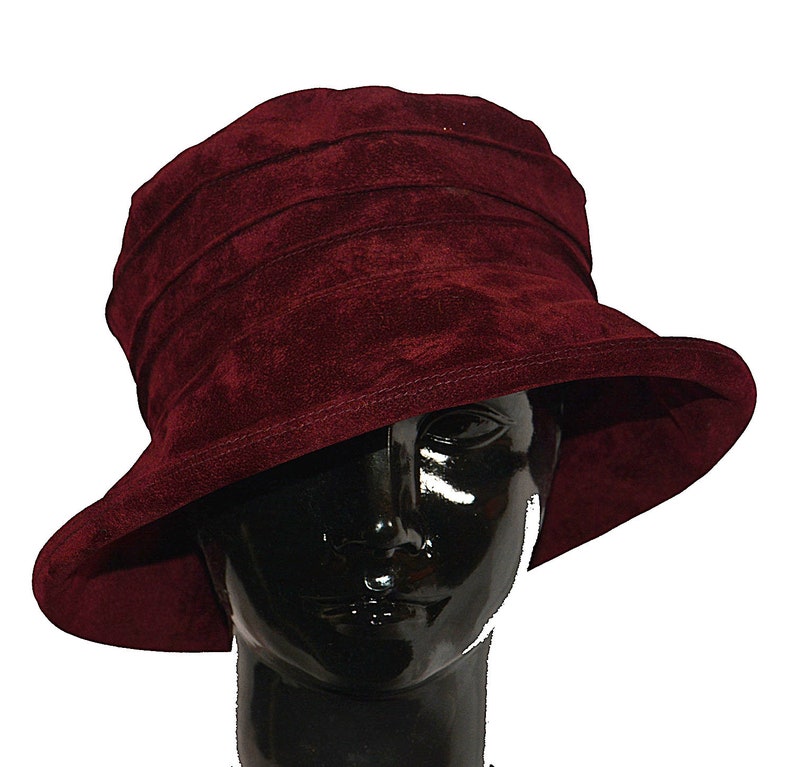 May include: A burgundy velvet cloche hat with a wide brim. The hat is folded in a series of pleats and has a simple, elegant design.