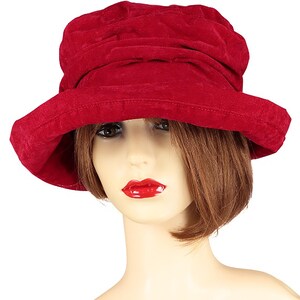 May include: A red velvet cloche hat with a wide brim. The hat is made of soft, textured fabric and has a slightly slouchy fit.