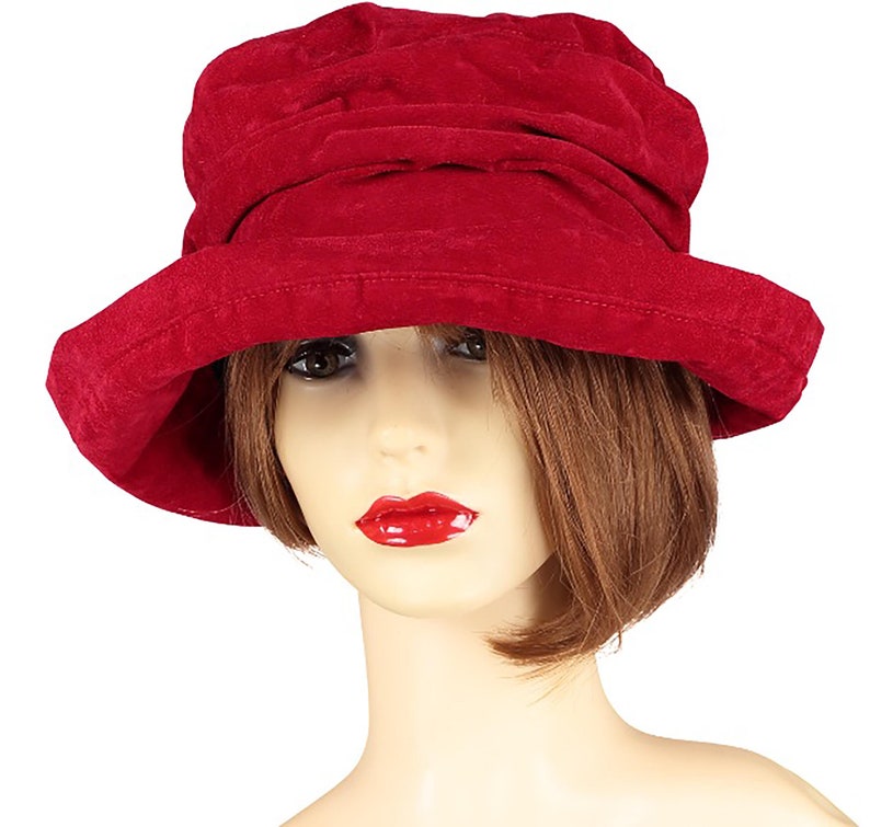 May include: A red velvet cloche hat with a wide brim. The hat is made of soft, textured fabric and has a slightly slouchy fit.