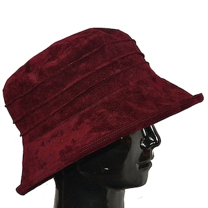 May include: A burgundy velvet bucket hat with a wide brim. The hat is made of soft, plush fabric and has a classic, timeless design.