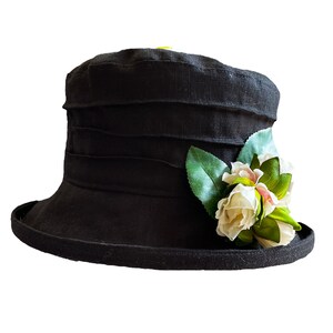 Puede incluir: Un sombrero de lino negro con ala ancha y una flor blanca.