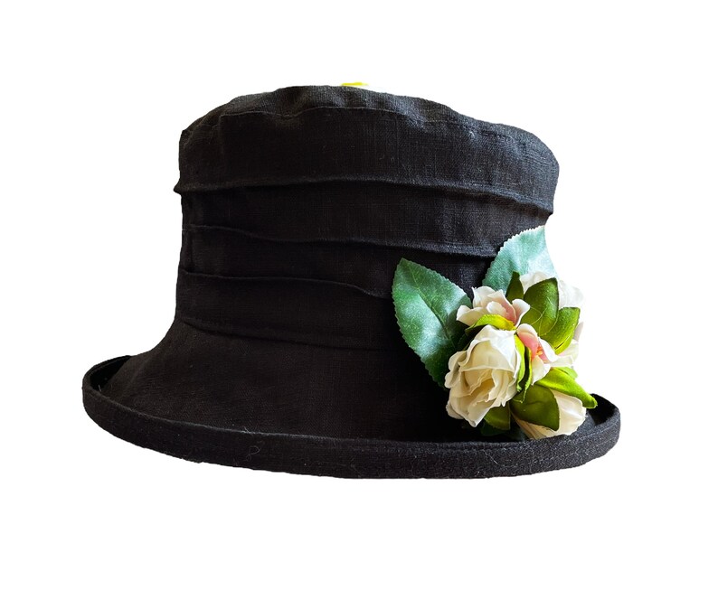 Puede incluir: Un sombrero de lino negro con ala ancha y una flor blanca.
