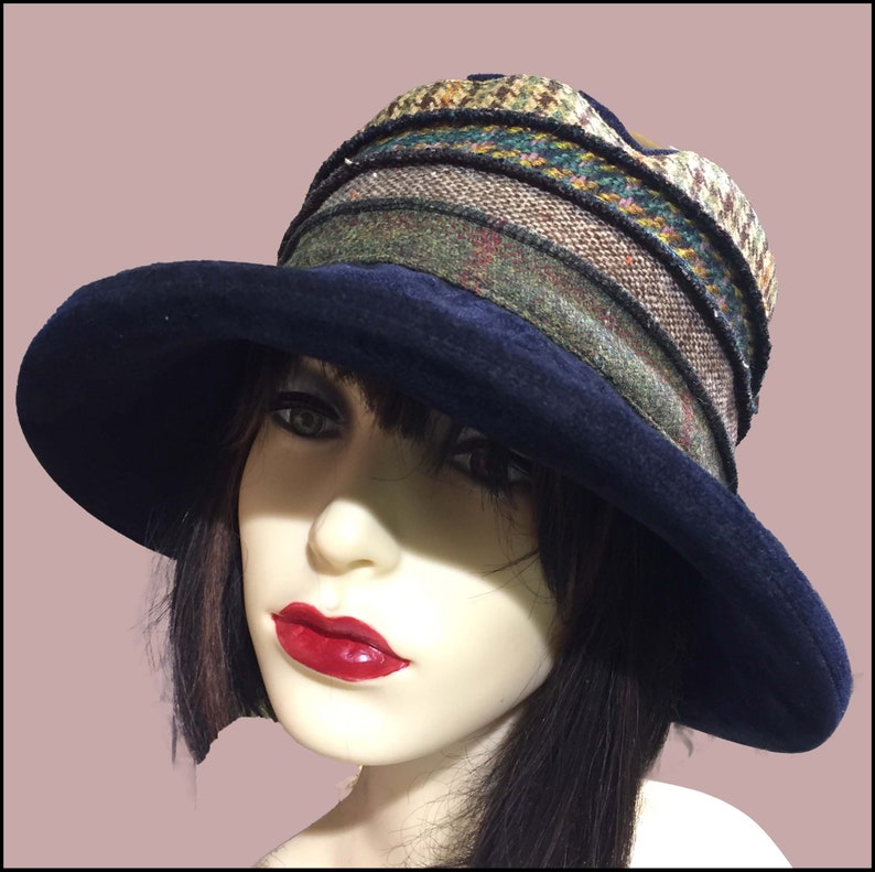 May include: A wide-brimmed hat with a navy blue velvet crown and a multi-colored patterned brim. The brim is made of a tweed fabric with a variety of colors and textures.