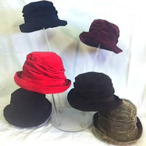 May include: Five felt hats displayed on a clear stand. The hats are in various colors, including black, red, burgundy, and brown.