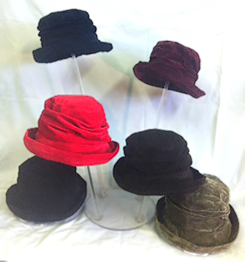 May include: Five felt hats displayed on a clear stand. The hats are in various colors, including black, red, burgundy, and brown.
