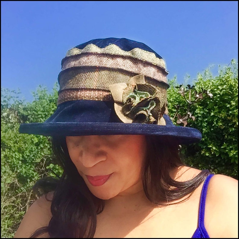May include: A navy blue velvet hat with a wide brim and a decorative flower accent. The hat has a multi-colored patterned band around the crown.
