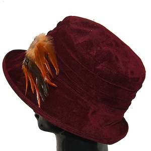 May include: A burgundy velvet hat with a brown and orange feather accent.