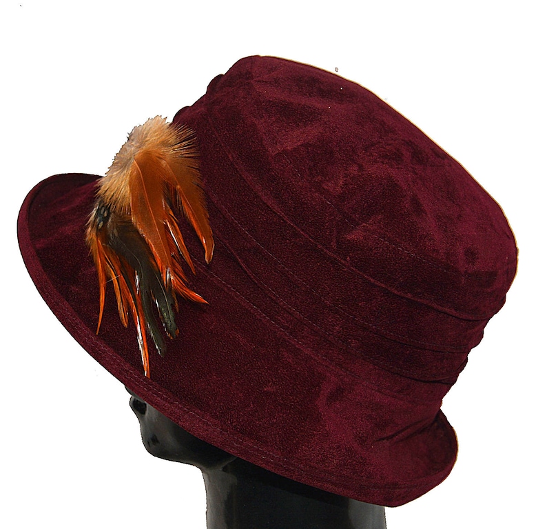 May include: A burgundy velvet hat with a brown and orange feather accent.