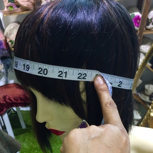 Puede incluir: Una cinta m&eacute;trica blanca est&aacute; envuelta alrededor de la cabeza de un maniqu&iacute;, mostrando una medida de 56 cm. La cinta est&aacute; sujeta por una mano.