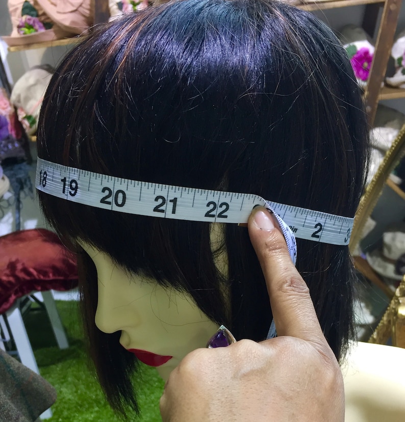 Puede incluir: Una cinta m&eacute;trica blanca est&aacute; envuelta alrededor de la cabeza de un maniqu&iacute;, mostrando una medida de 56 cm. La cinta est&aacute; sujeta por una mano.
