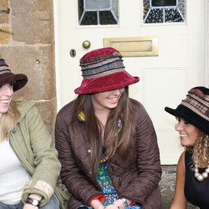 Puede incluir: Tres mujeres con sombreros de diferentes patrones. Los sombreros son todos de tela y tienen un ala ancha. Las mujeres sonr&iacute;en y miran a la c&aacute;mara.