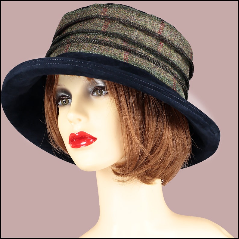 May include: A black and green tweed hat with a black velvet brim. The hat has a wide brim and a simple design.