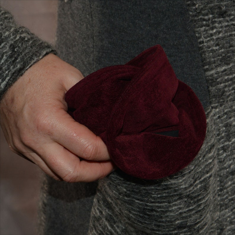 May include: A hand holding a folded burgundy velvet fabric hat.