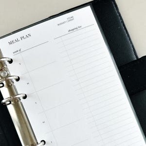 May include: A white meal planner page with a black binder. The page has a section for a meal plan, a shopping list, and a budget/spent section. The page is labeled "Meal Plan" and has a section for each day of the week. The page is from Simply Your Jessica.
