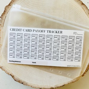 May include: A white sheet of paper with the text 'CREDIT CARD PAYOFF TRACKER' at the top. Below the text are 40 small black and white credit card icons arranged in 5 rows of 8. The sheet also has the text 'Starting Balance:' and 'Card:' at the bottom. The sheet is in a clear plastic zippered pouch.
