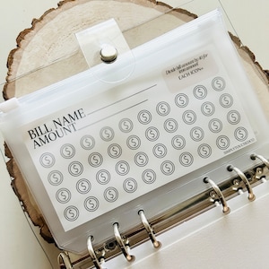 May include: A clear plastic pouch with a zipper closure, labeled "BILL NAME AMOUNT". The pouch contains a sheet of dollar sign icons, with a note that reads "Divide bill amount by 40 for each icon".