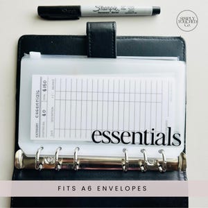 May include: A clear plastic envelope with a white card inside. The card has a grid pattern and the text "CATEGORY essentials STARTING BAL $0 GOAL $150 BALANCE" printed on it. The envelope is labeled "essentials" in black text. The envelope fits A6 envelopes.