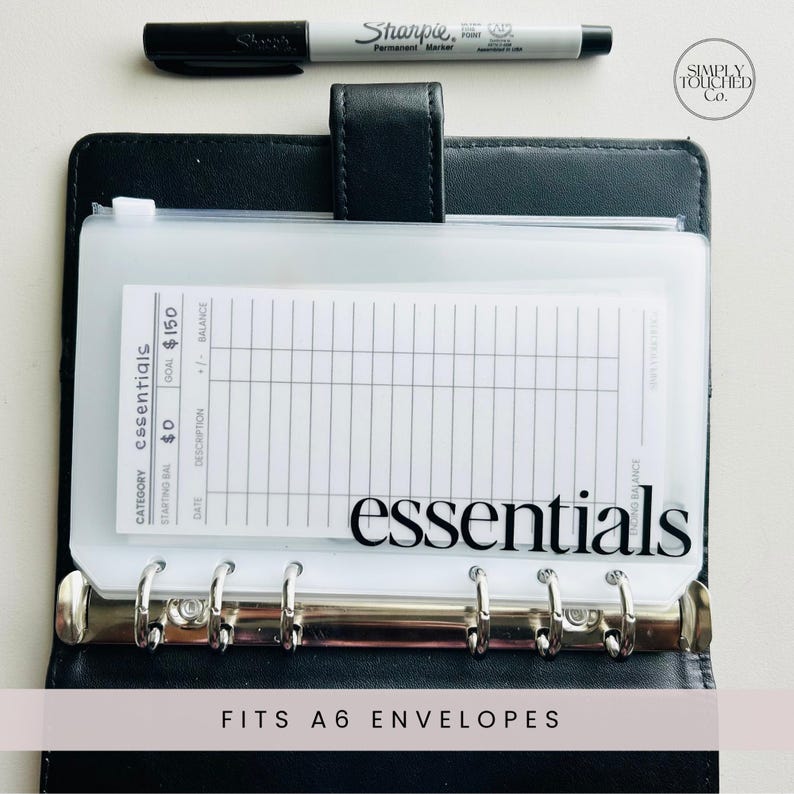 May include: A clear plastic envelope with a white card inside. The card has a grid pattern and the text "CATEGORY essentials STARTING BAL $0 GOAL $150 BALANCE" printed on it. The envelope is labeled "essentials" in black text. The envelope fits A6 envelopes.