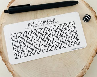 May include: A white card with the text "Roll the Dice Savings Challenge" and a grid of 36 dice with different numbers of dots. The card is on a wooden surface with a black pen and a black dice.