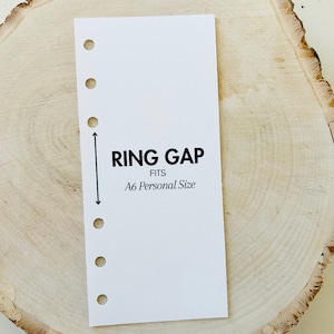 May include: White card with black text that reads "RING GAP FITS A6 Personal Size". The card has six holes along the left edge and a vertical line with arrows pointing up and down.