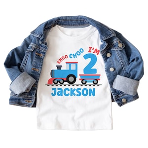 May include: White t-shirt with a blue train and red caboose, the words "Choo Choo I'm 2" and the name "Jackson" printed on it.