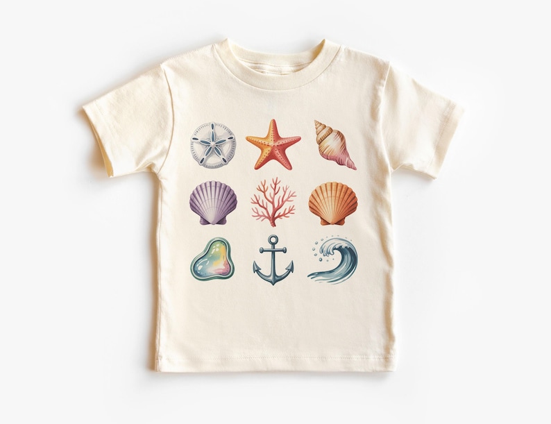 May include: A cream-colored t-shirt featuring a collection of watercolor illustrations of marine life. The design includes a starfish, seashells, coral, an anchor, and a wave. The shirt is a short-sleeved style.
