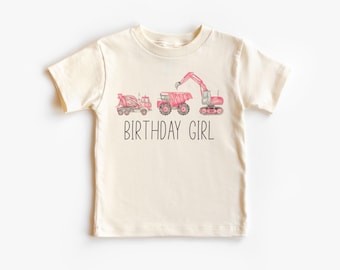 May include: A cream-colored short-sleeved t-shirt with a pink and gray illustration of construction vehicles and the text "Birthday Girl".