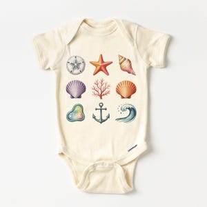 May include: Cream-colored baby onesie featuring watercolor illustrations of various sea elements. The design includes a starfish, seashells, coral, an anchor, and a wave. The illustrations are in shades of orange, purple, and blue.