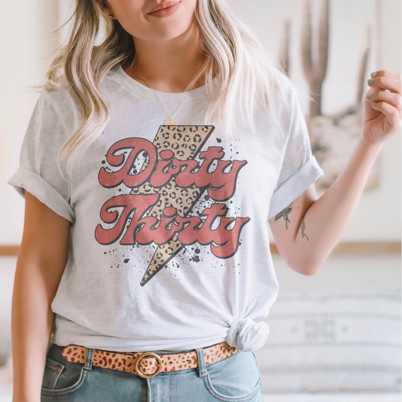 May include: A white t-shirt with a red and yellow lightning bolt graphic. The graphic has a leopard print design and the text "Dirty Thirty" in a retro font.