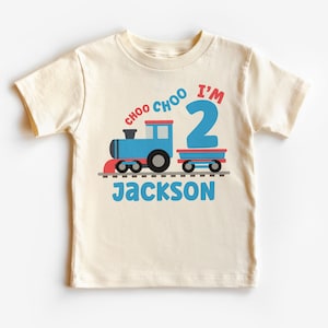 May include: A cream colored t-shirt with a blue train and red caboose. The train says "Choo Choo I'm 2" and the name "Jackson" is printed below the train.